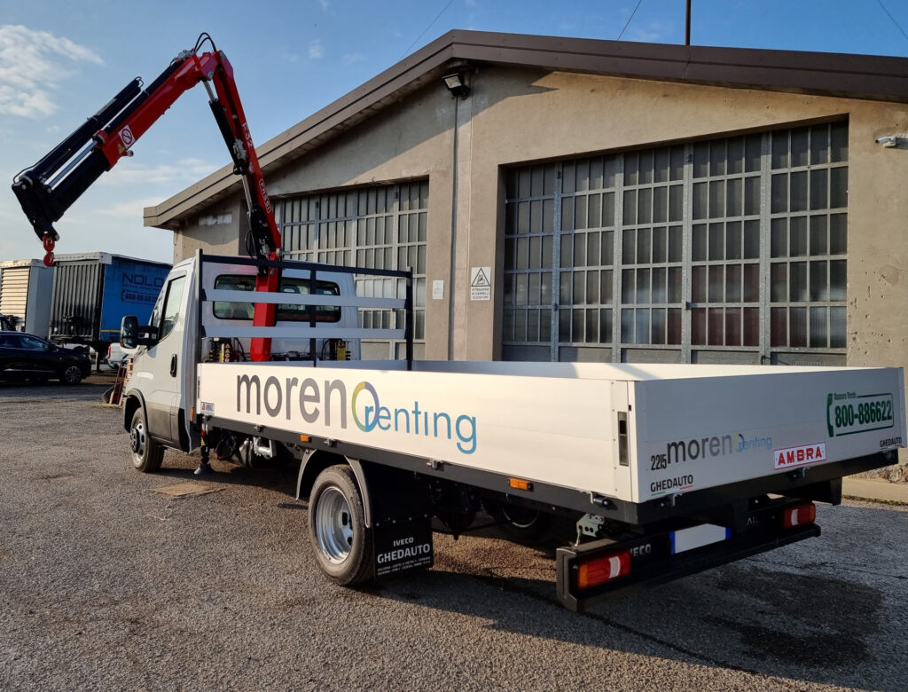 Camioncino cassonato con gru idraulica estesa, disponibile a noleggio per sollevamento e trasporto materiali in edilizia.